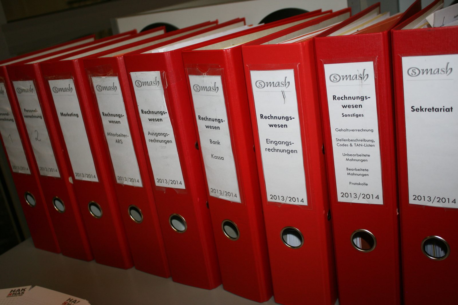 Rząd tekturowych segregatorów i teczek z dokumentami ustawionych na półce — obraz biurokratycznego archiwum akt.